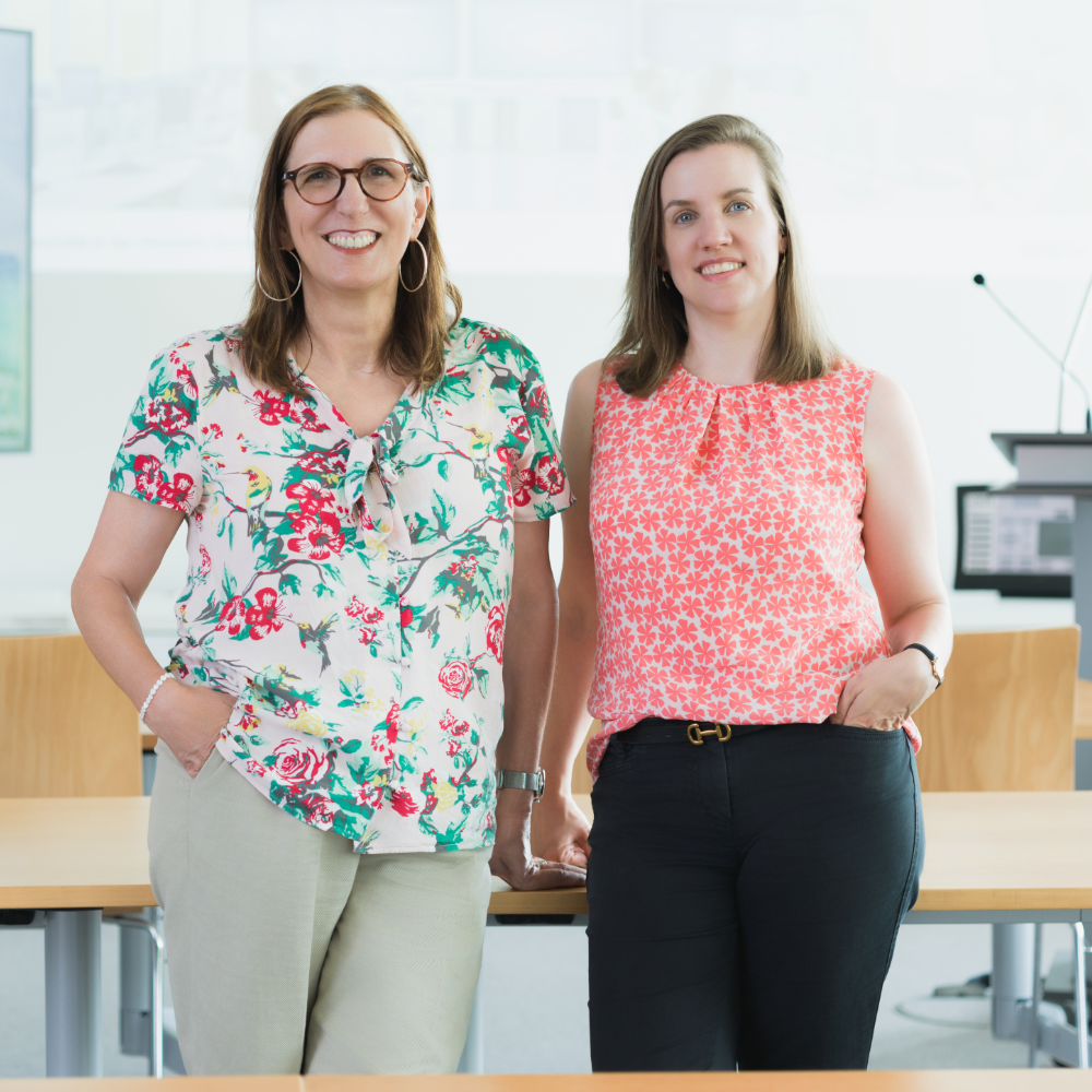 Two women standing side by side in an indoor setting, wearing floral tops.