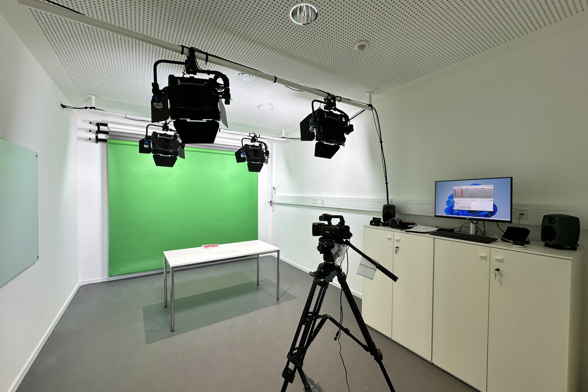 Studio mit Greenscreen, Kamera auf Stativ, Monitor und Beleuchtungsausrüstung.
