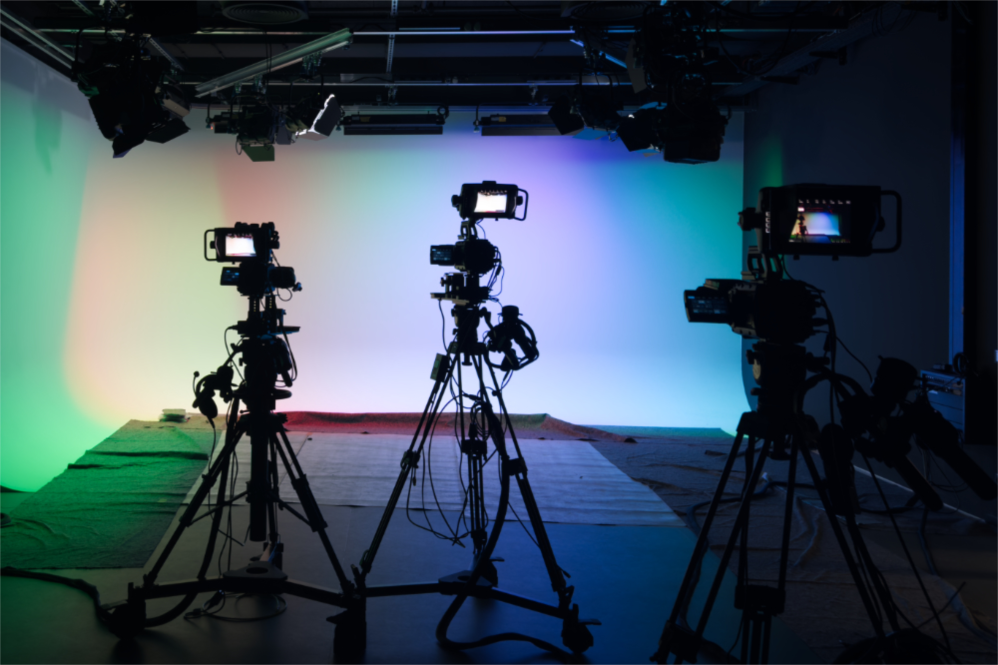 Drei Kameras im Studio vor mehrfarbig beleuchtetem Hintergrund.